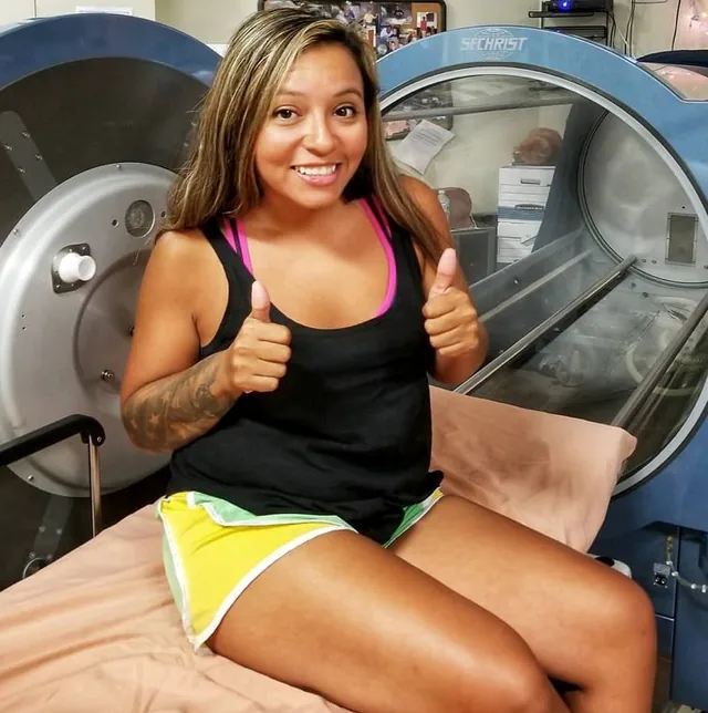 Veteran giving a thumbs up beside an HBOT chamber